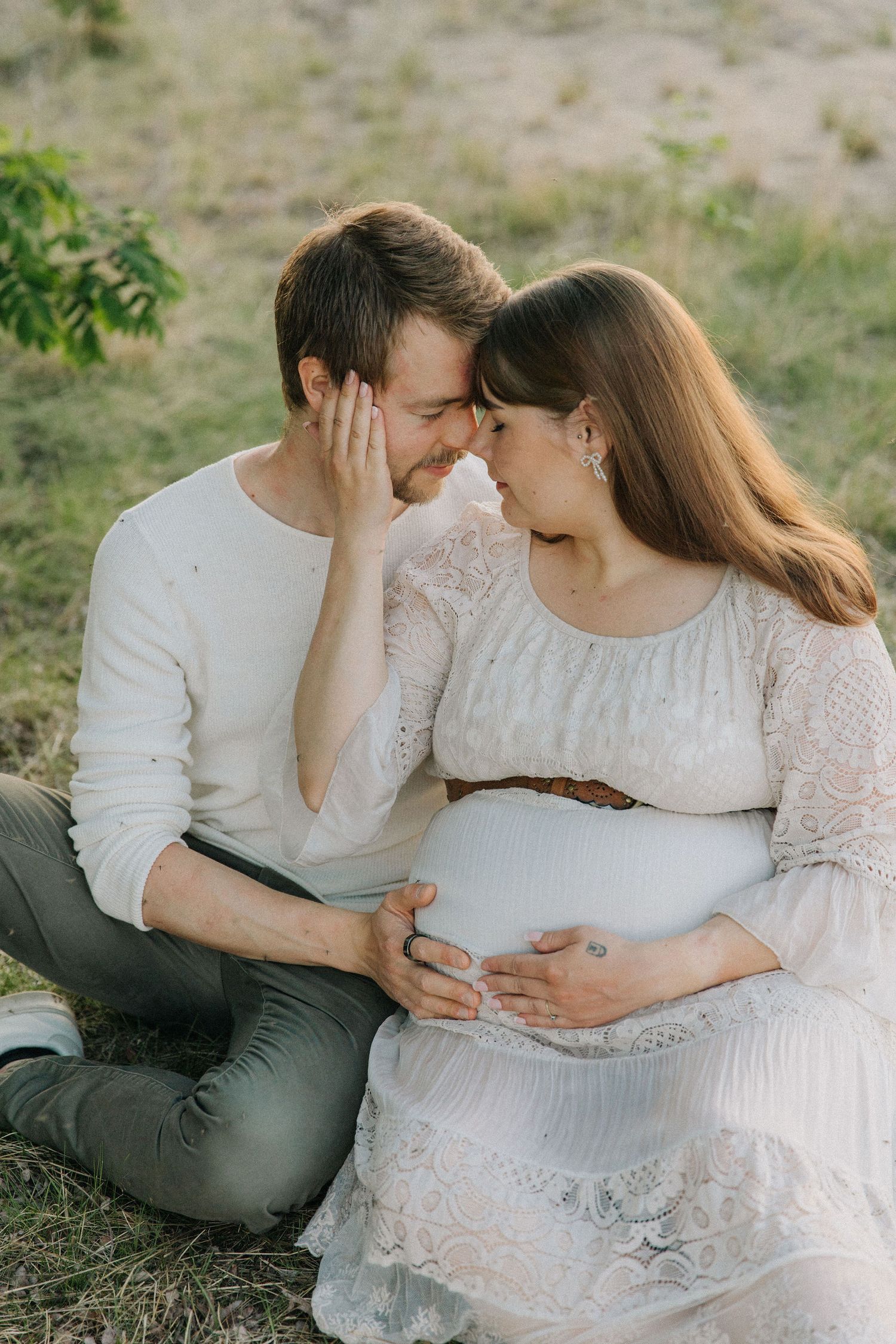 Intimate maternity photo of couple sharing tender moment outdoors in white attire.