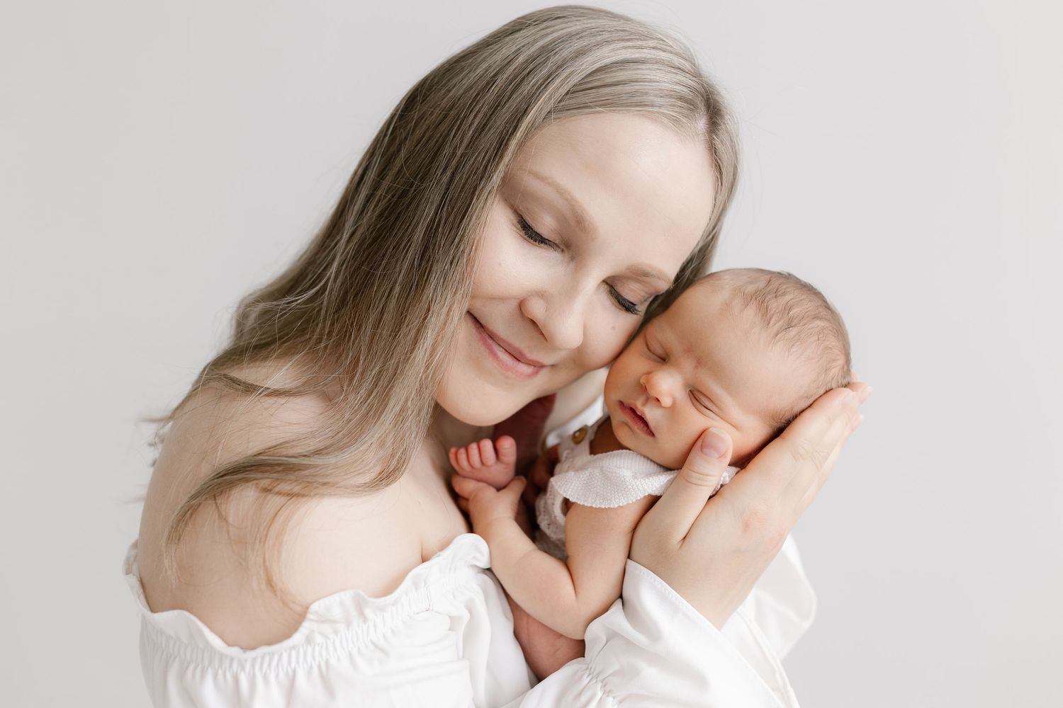 Tender moment between parent and baby in soft white tones captured in a series of intimate portraits.