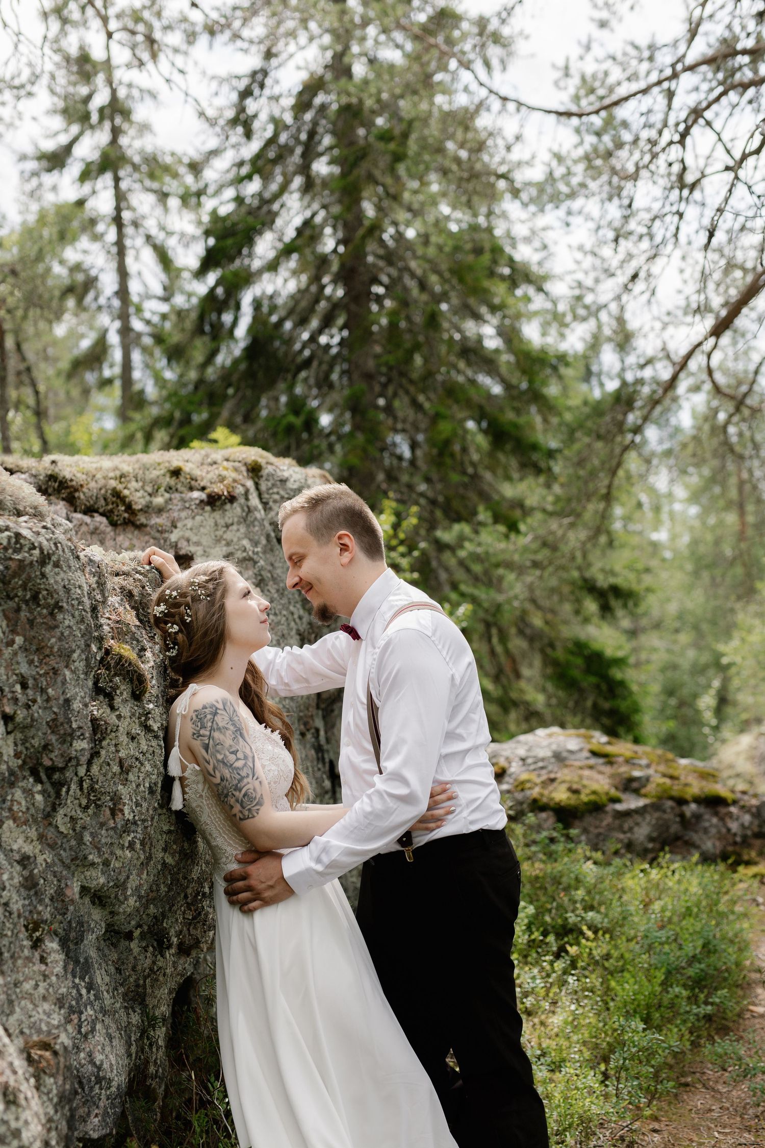 Romantic outdoor wedding portrait against a large moss-covered rock in a forest setting.