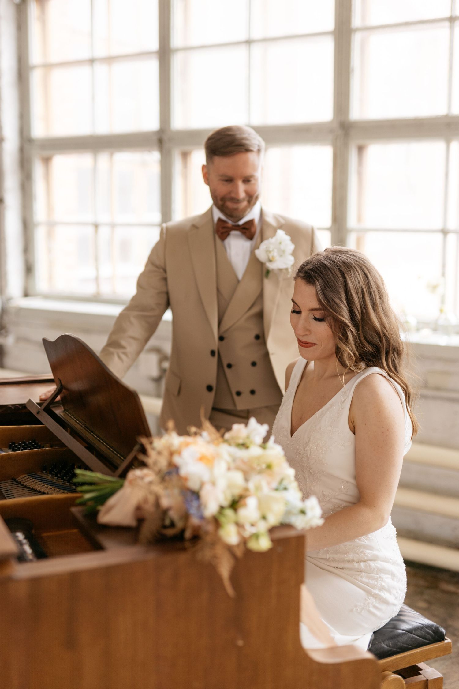 Couple in formal attire sharing a romantic moment at a piano during their wedding.