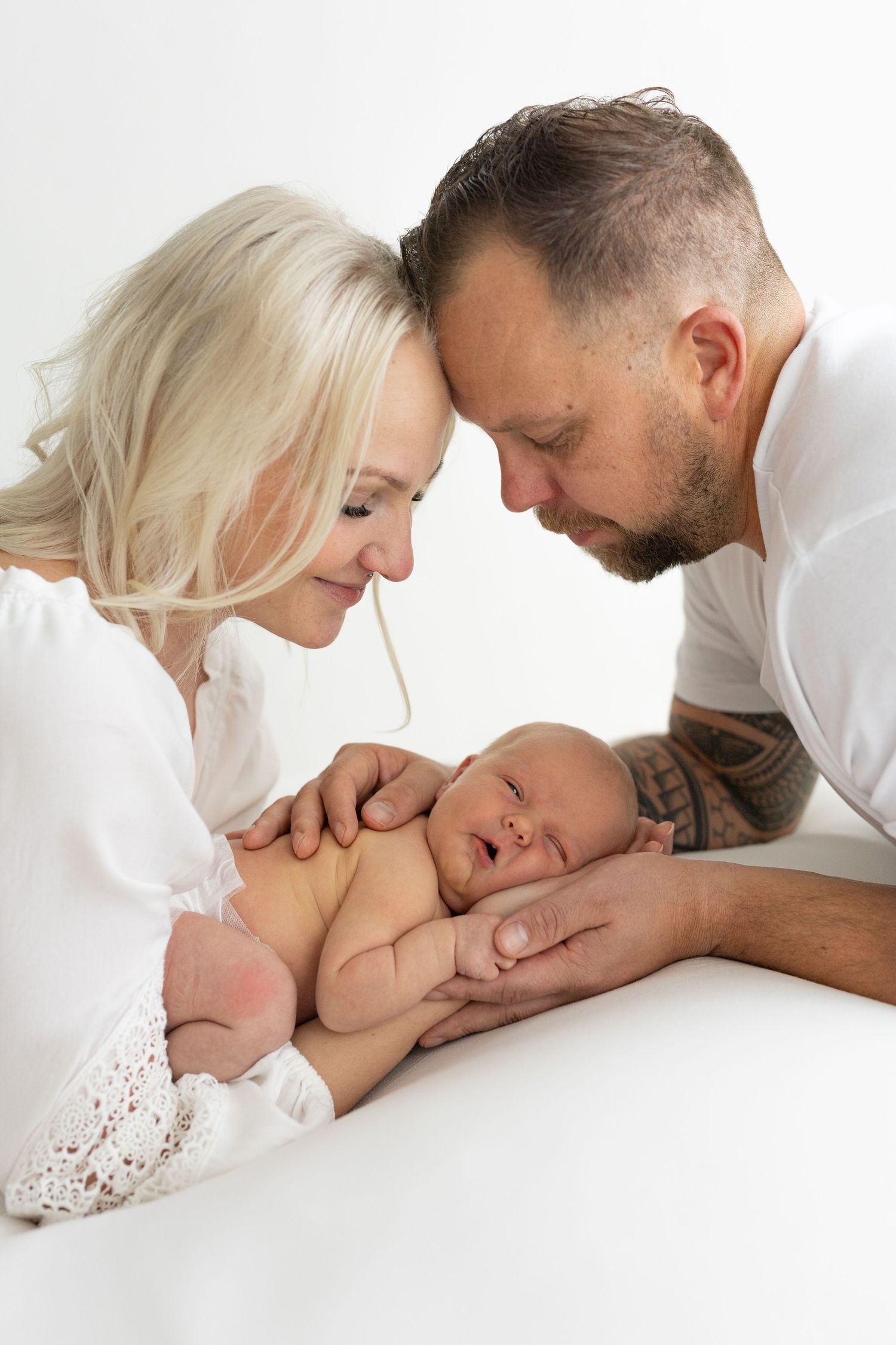 Parents lovingly gazing at their sleeping newborn on white background.