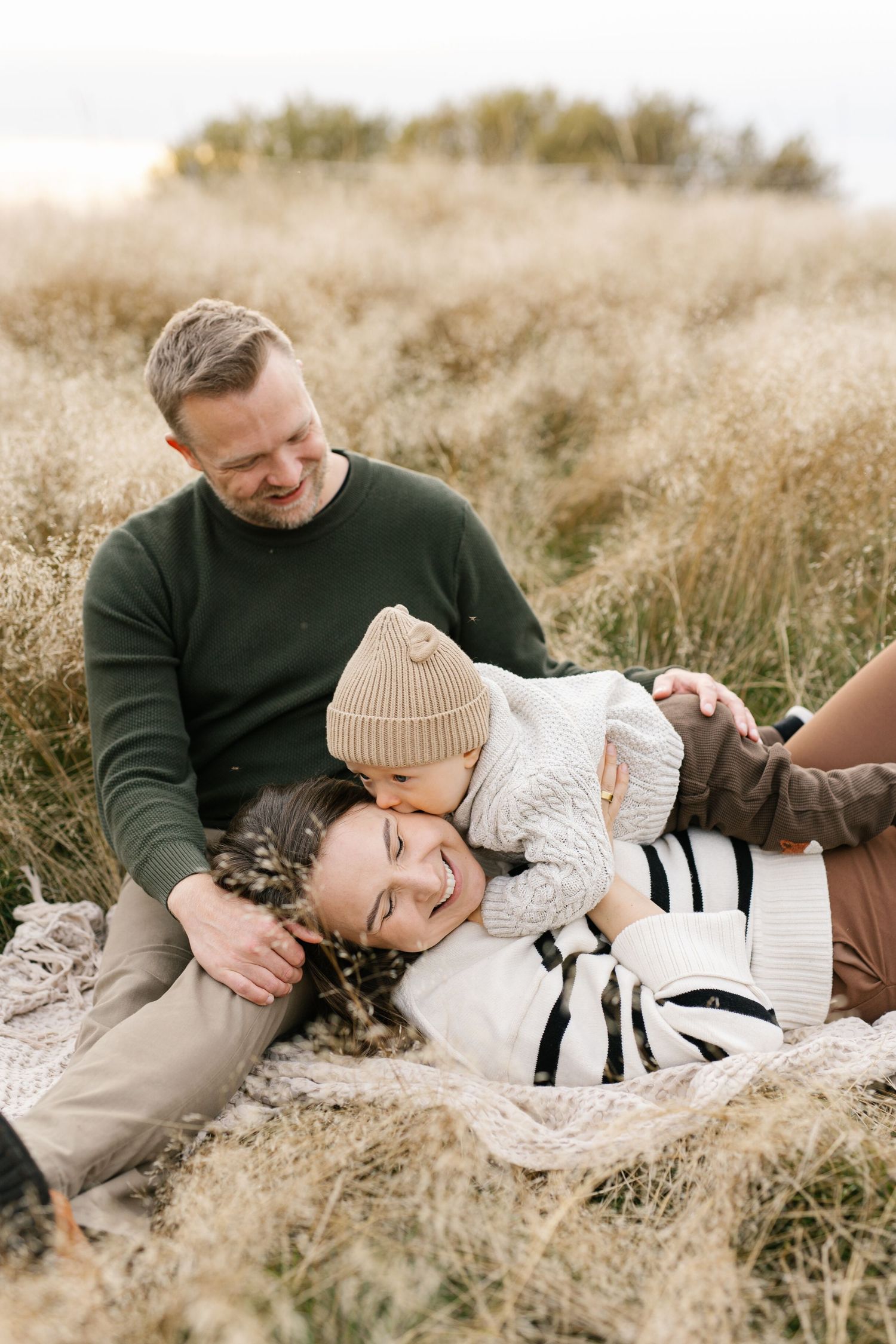 A family shares a tender moment while laying together on a blanket in tall autumn grass during a photo session.