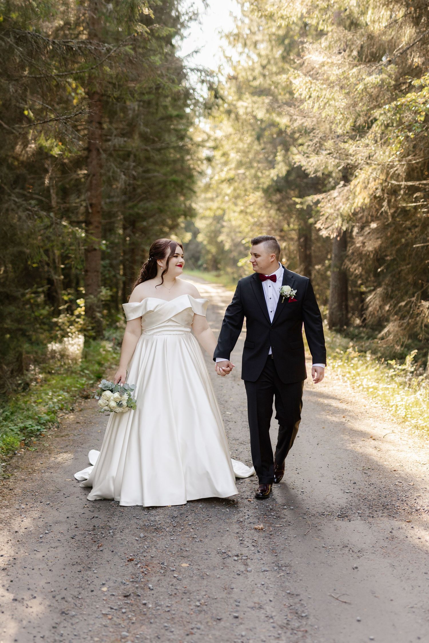 A couple walks hand in hand down a forest path on their wedding day.