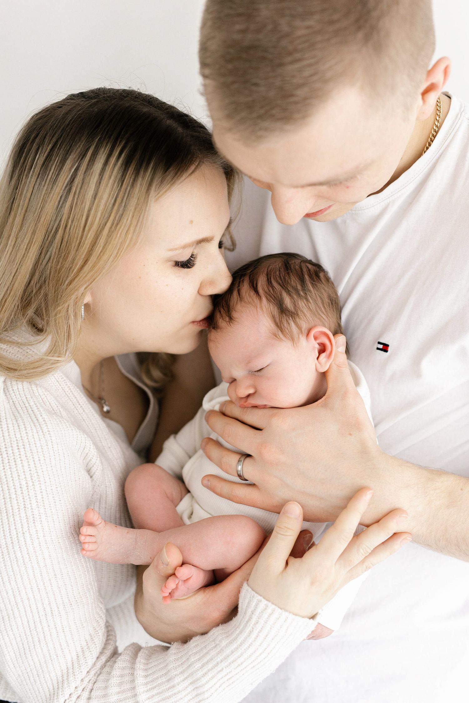 Parents cuddle newborn baby in tender moment against white background.