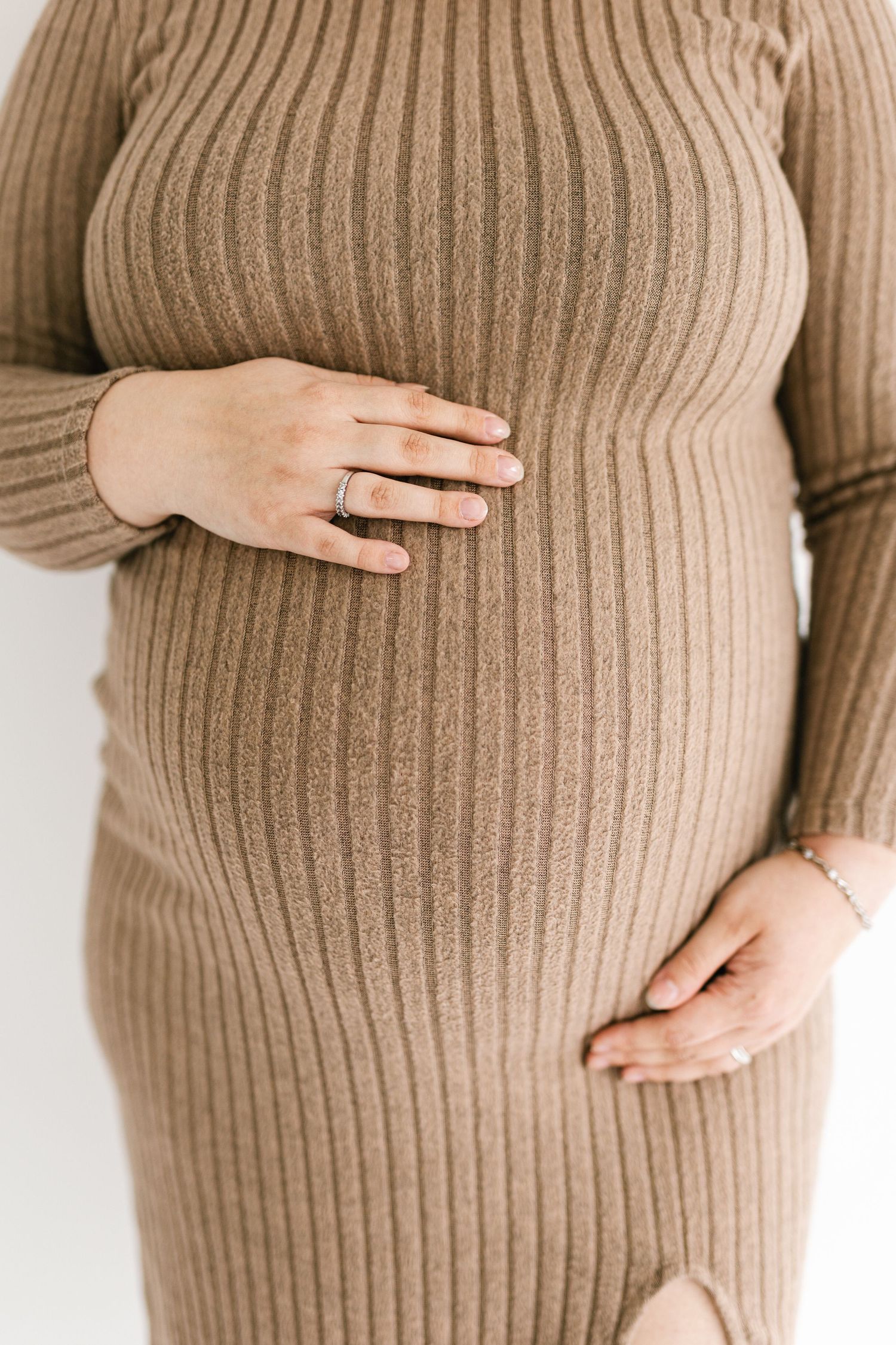 Close-up of pregnant belly in ribbed brown sweater with hands resting on top.