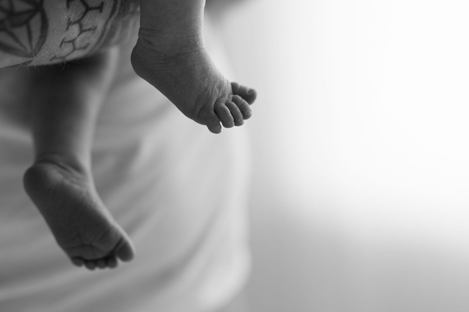 Black and white artistic close-up of tiny baby feet against bright background.