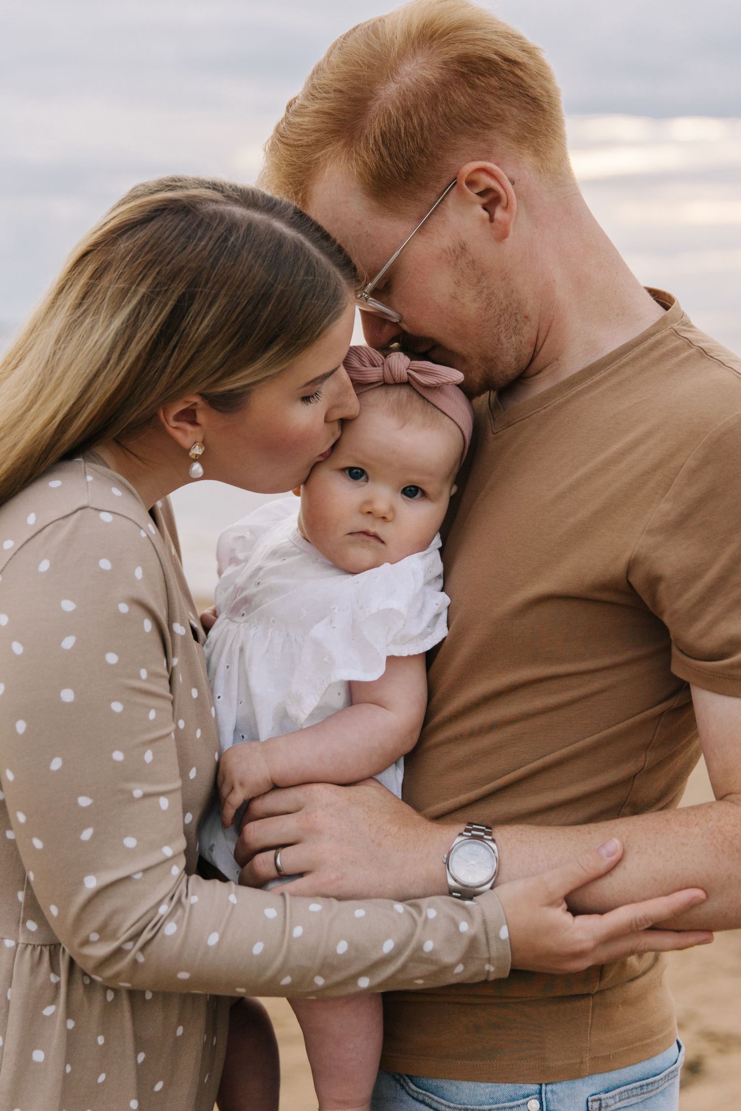 An intimate family moment captured on the beach with parents kissing their baby's head.