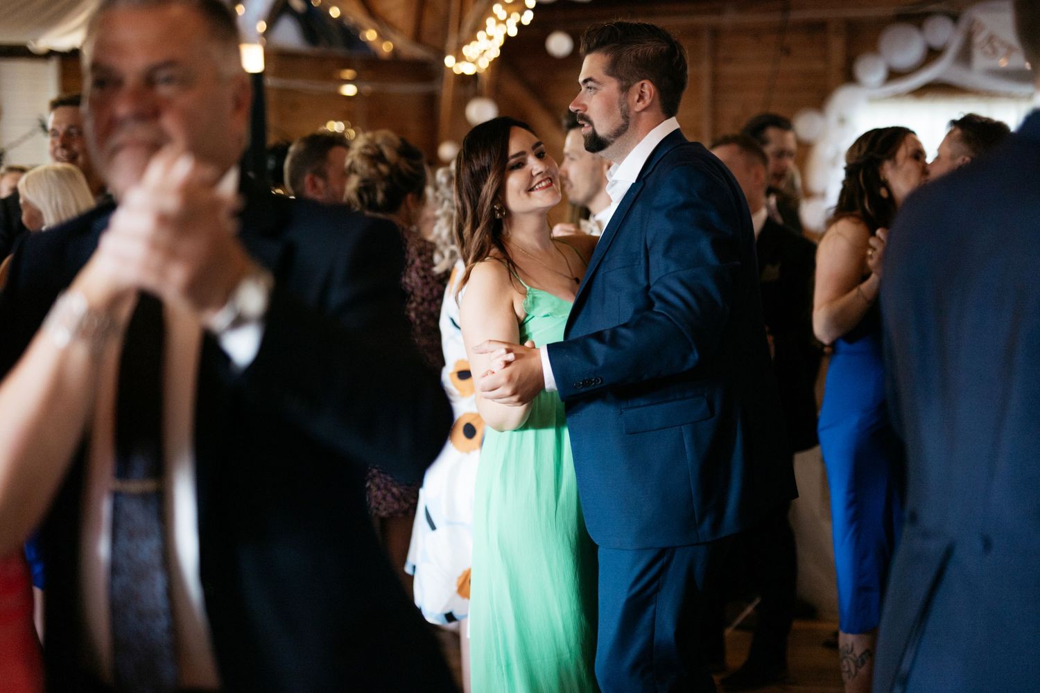 Couples dancing at a wedding reception in a rustic venue with string lights.