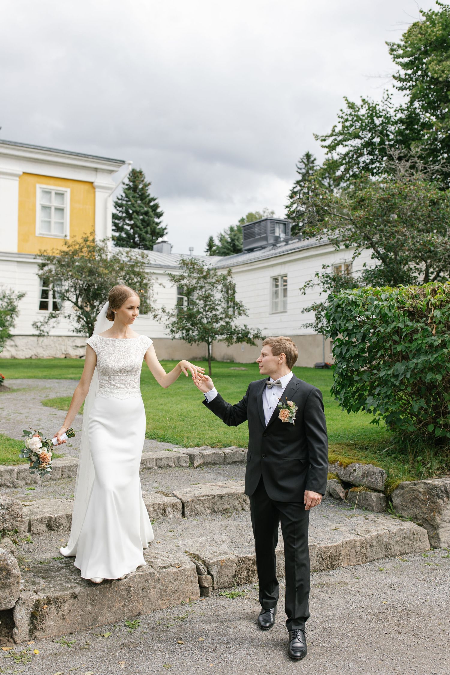 Bride and groom holding hands while walking on stone steps at elegant estate.