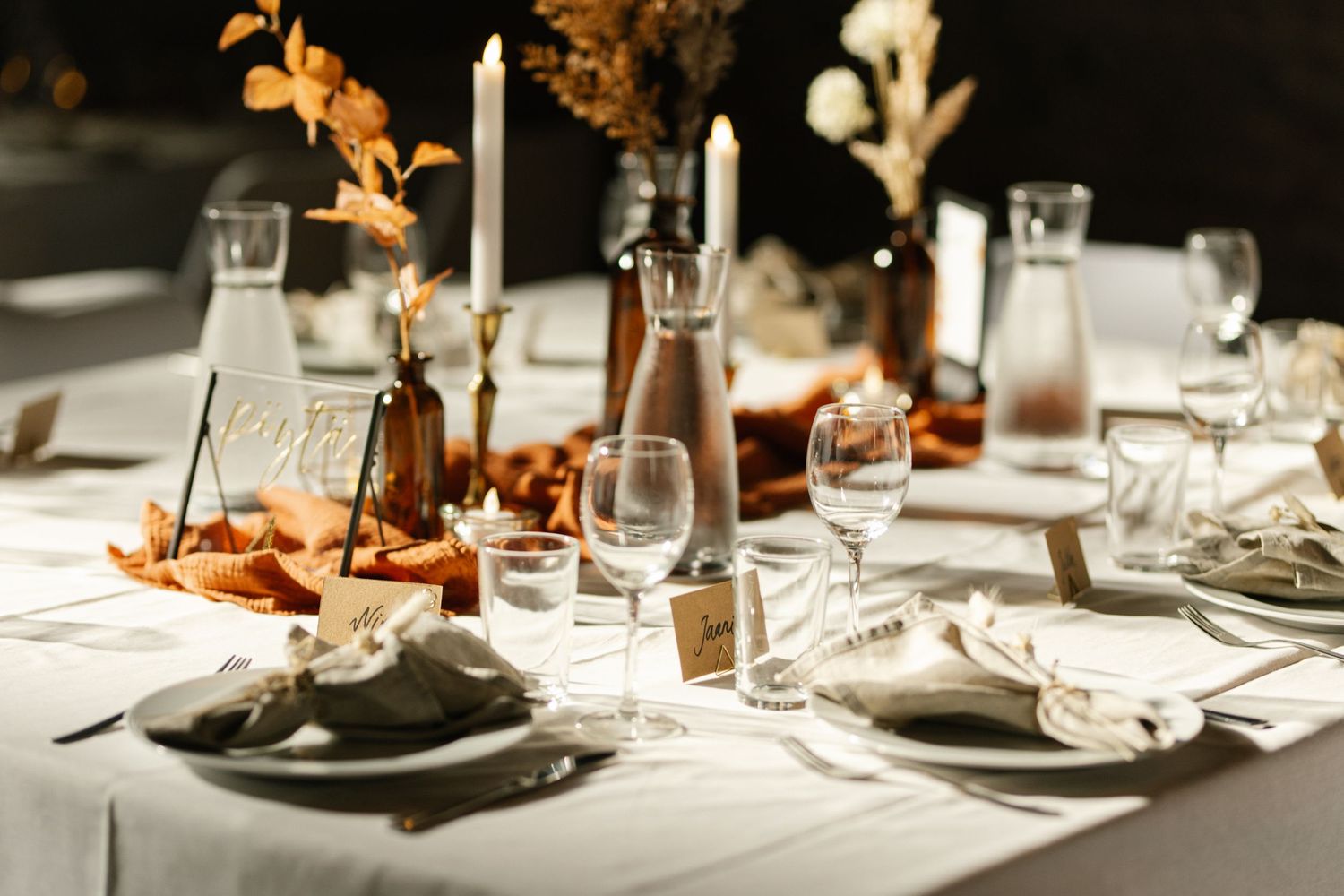 Elegant wedding reception table setting with white linens, candles and autumn-colored floral decorations.