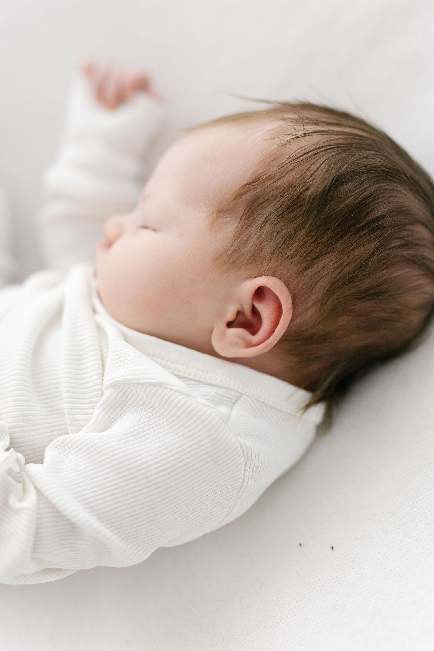 Sleeping baby in white onesie captured in profile view against white background.
