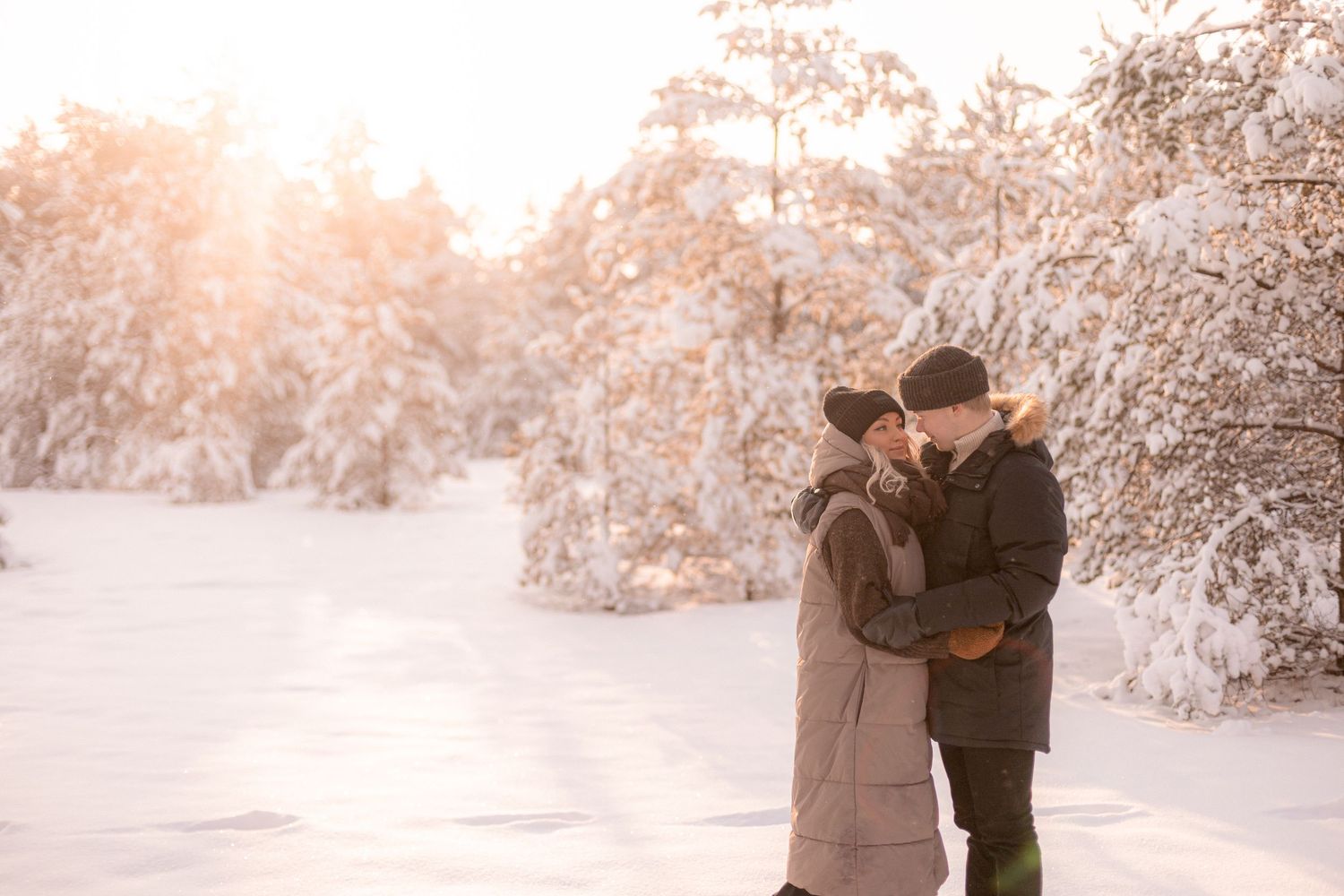 A couple embracing in a snowy winter wonderland during golden hour.