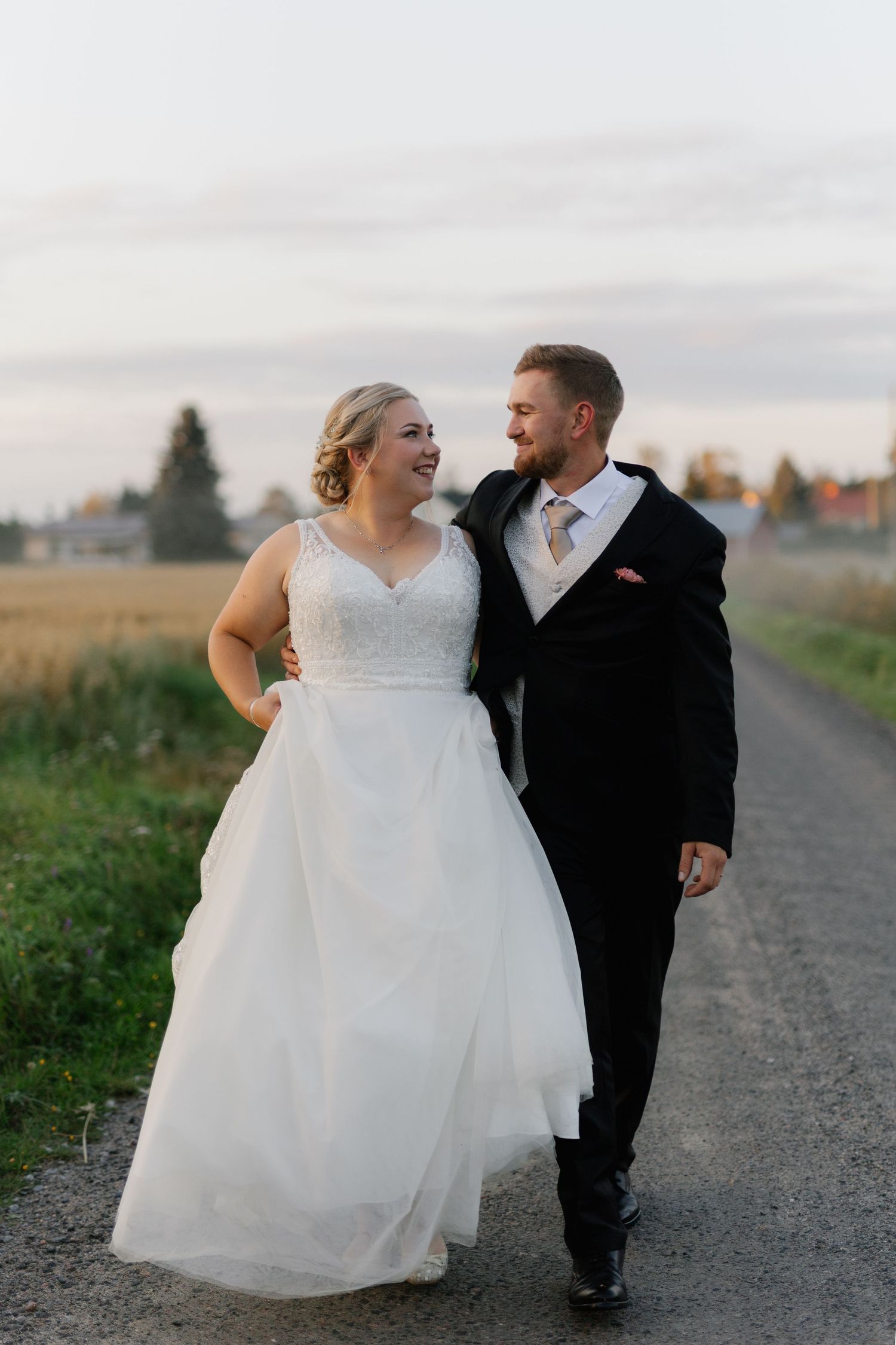 A joyful wedding couple walking and laughing together on country road.