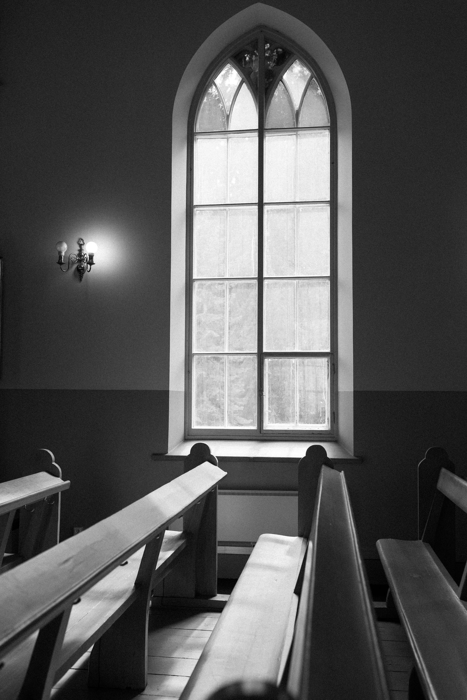 Interior view of a Gothic church window with wooden pews in black and white.