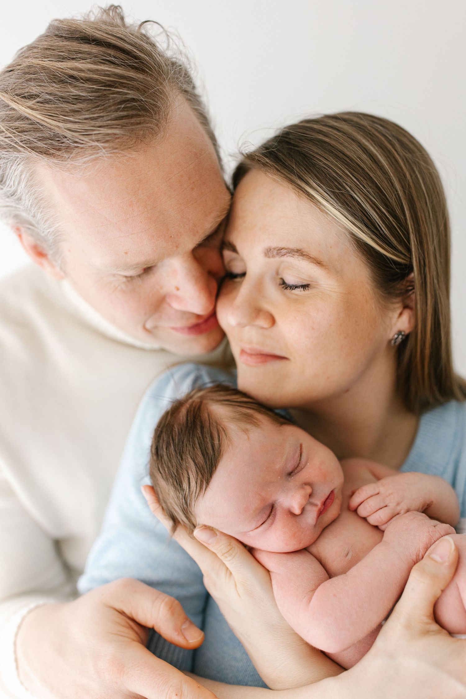 Tender moment between parents and sleeping newborn baby in soft natural light.