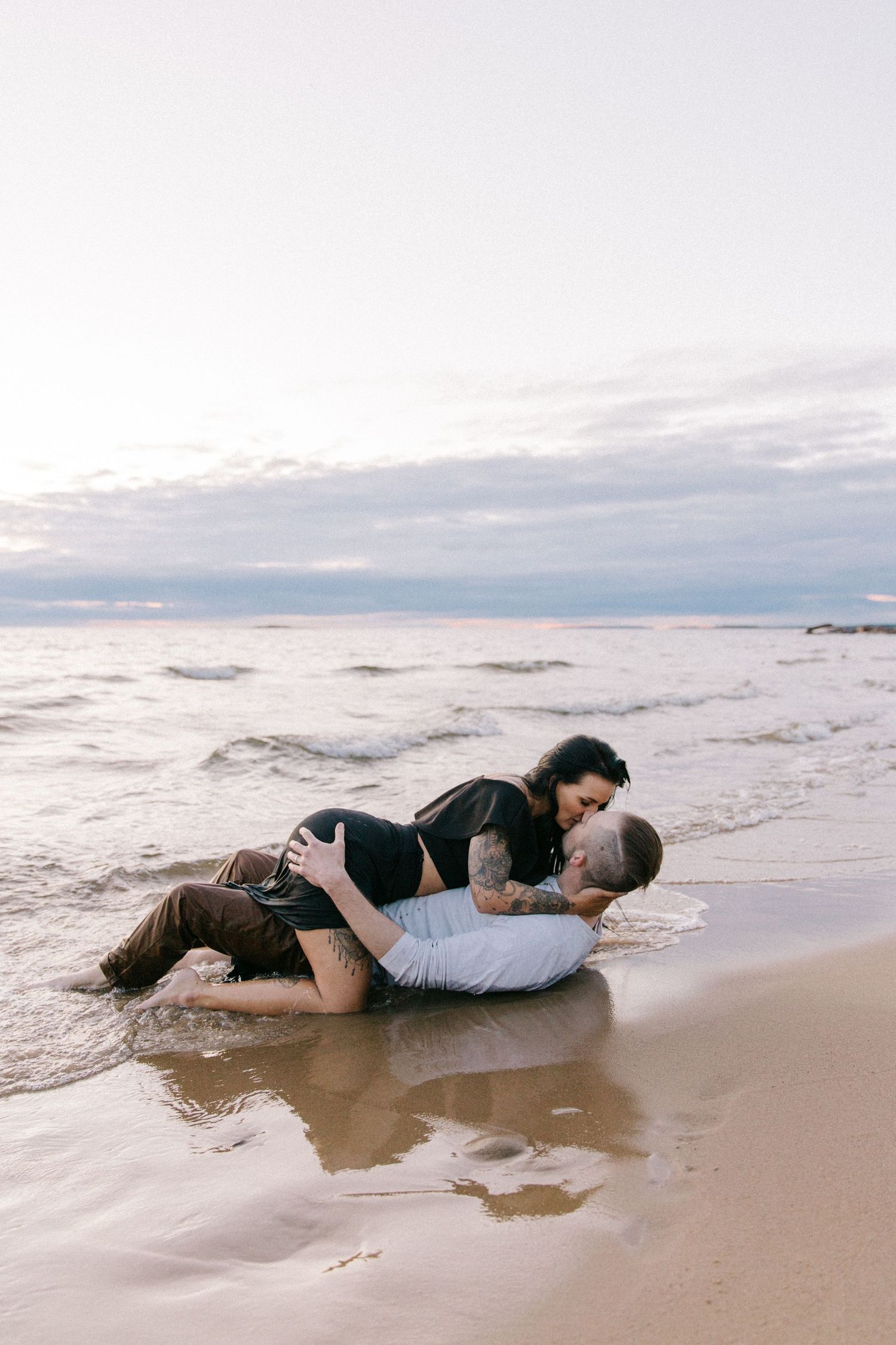 Couple embracing on sandy beach at sunset with waves in background.