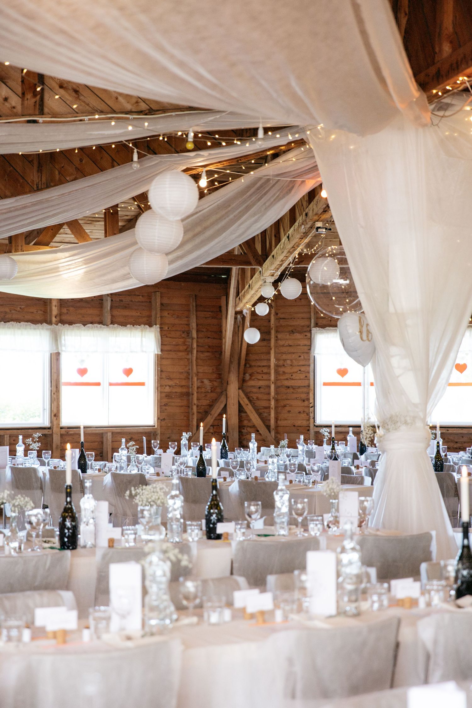 Elegant barn wedding reception with white draping, lanterns and romantic table settings.