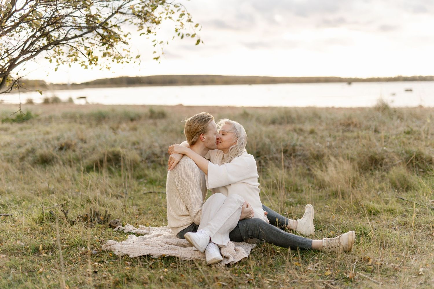 Cozy couple cuddling on blanket in grassy field at golden hour.