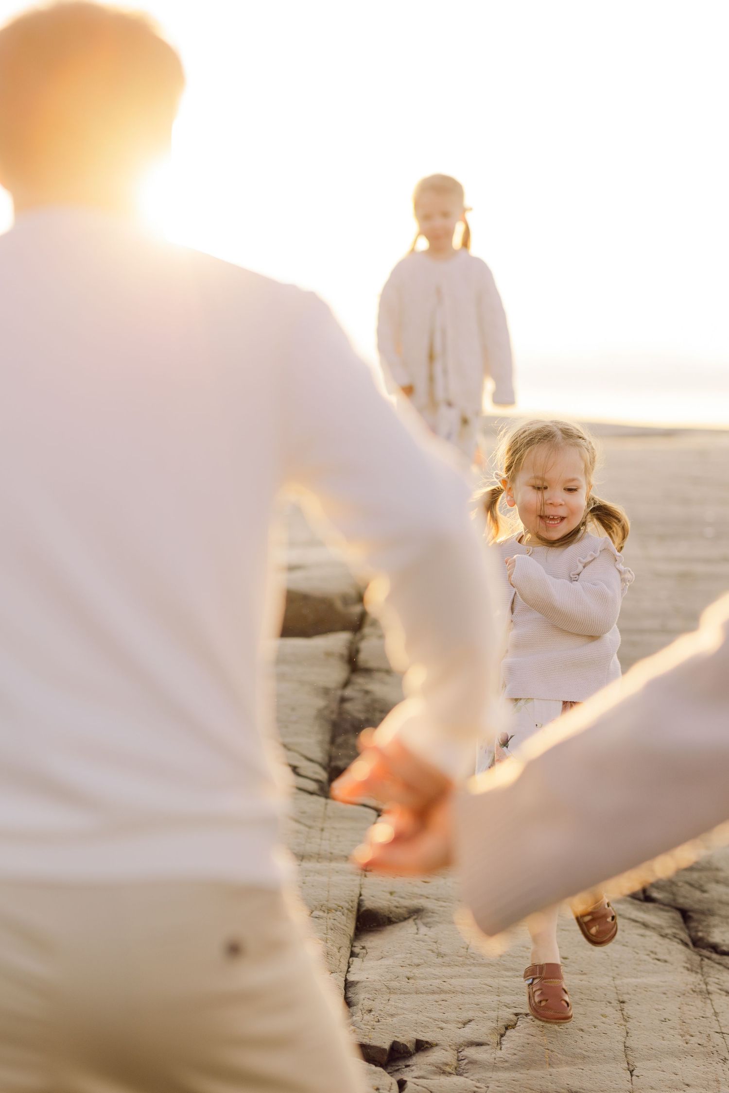Family wearing white outfits plays together at sunset on a beach during golden hour.