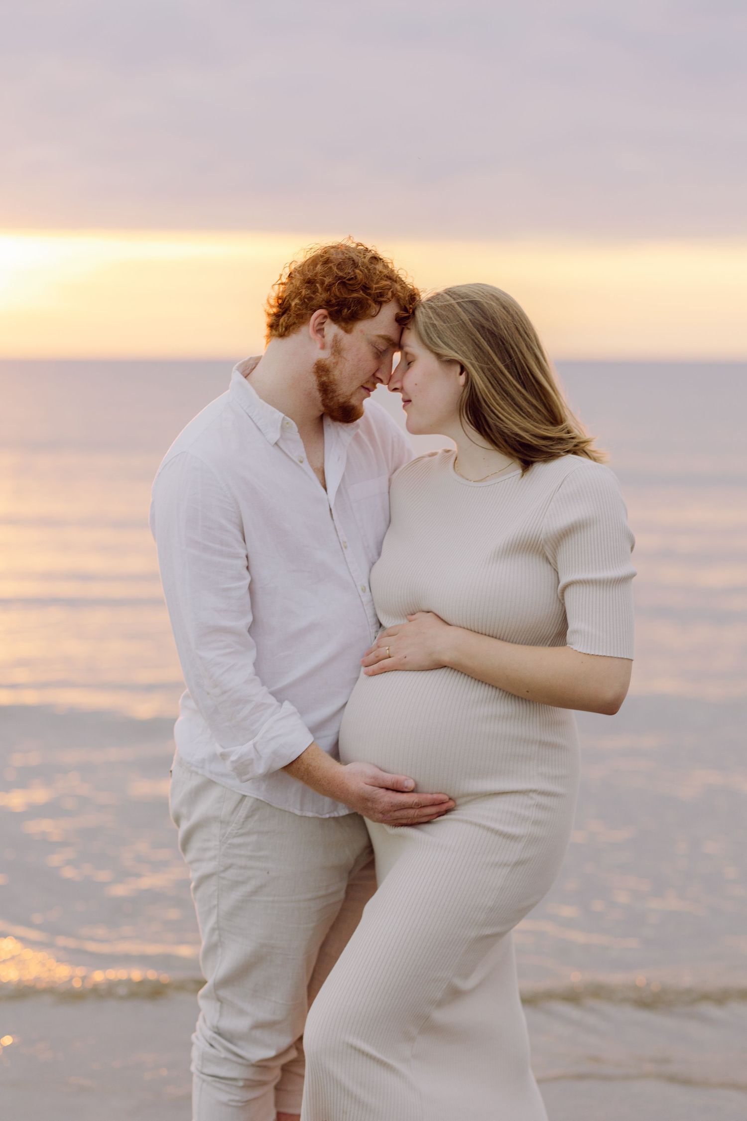 Intimate moment between couple on beach at sunset with warm golden lighting.