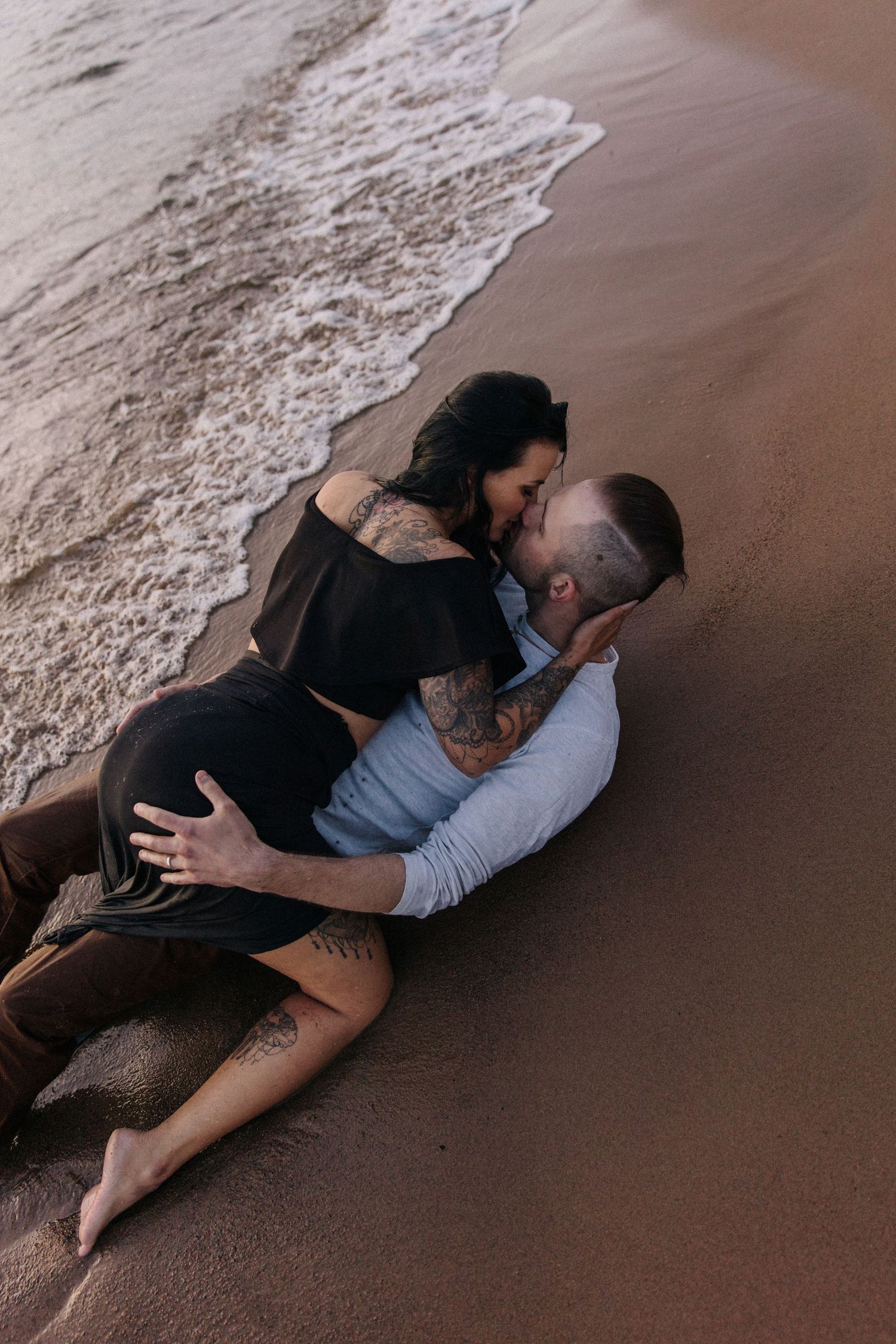 A couple embracing on the beach as waves lap at the shore during golden hour.