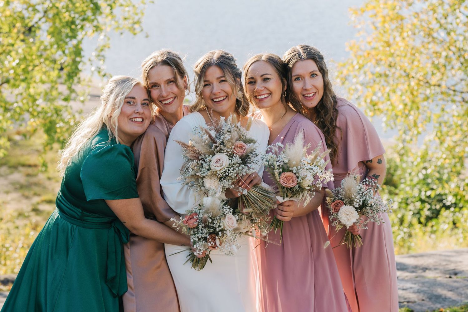 Bridal party in colorful dresses poses together with bouquets outdoors.