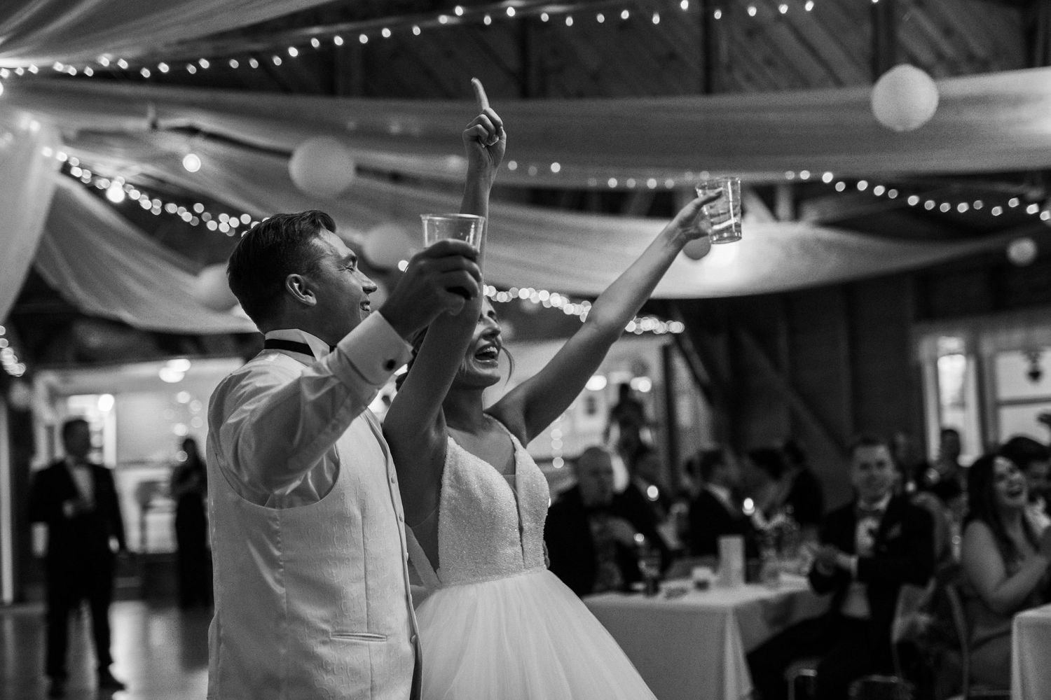 A black and white photo of newlyweds celebrating with raised arms on their wedding dance floor.