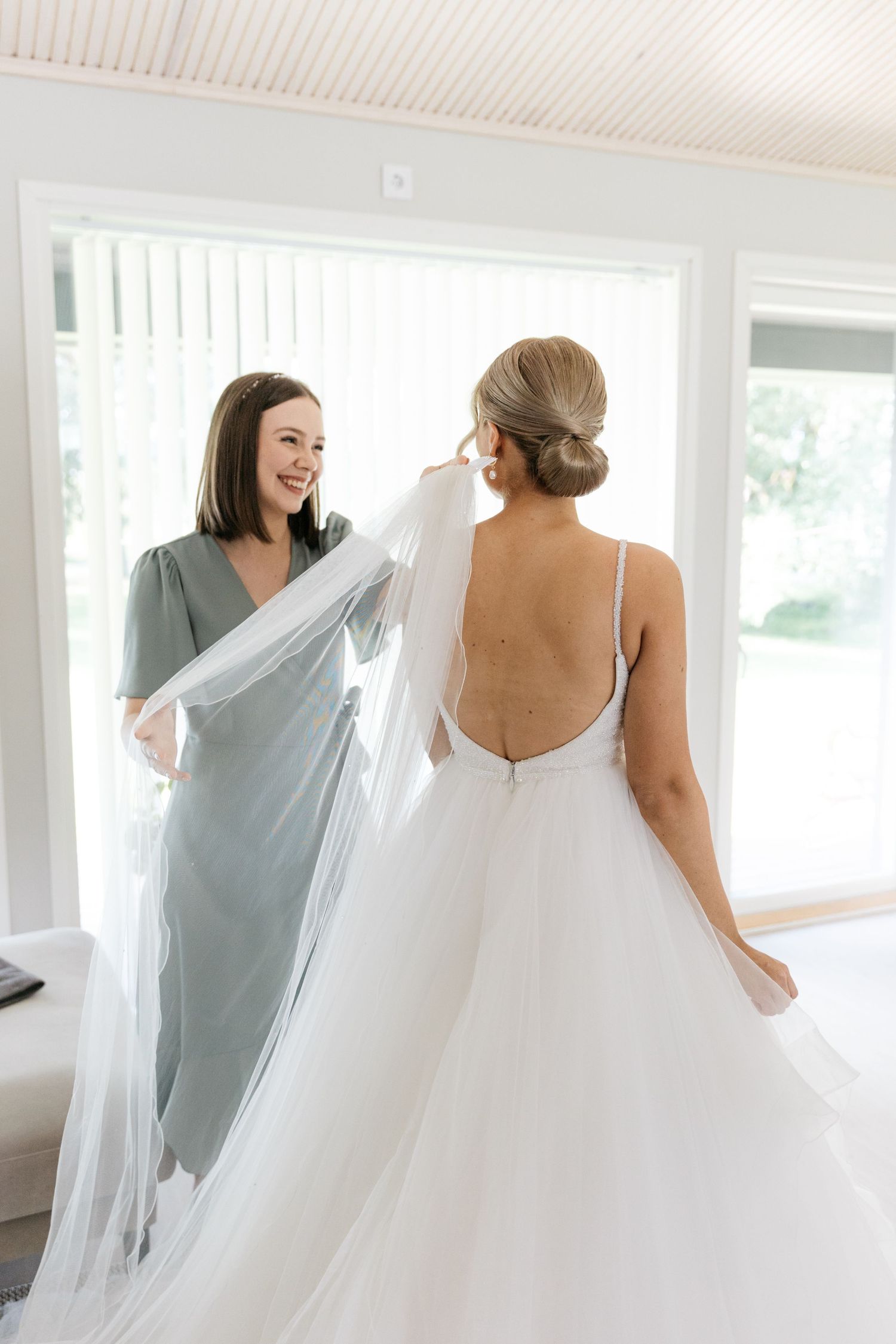 A flowing white wedding dress with an open back design being styled in a bright indoor setting.