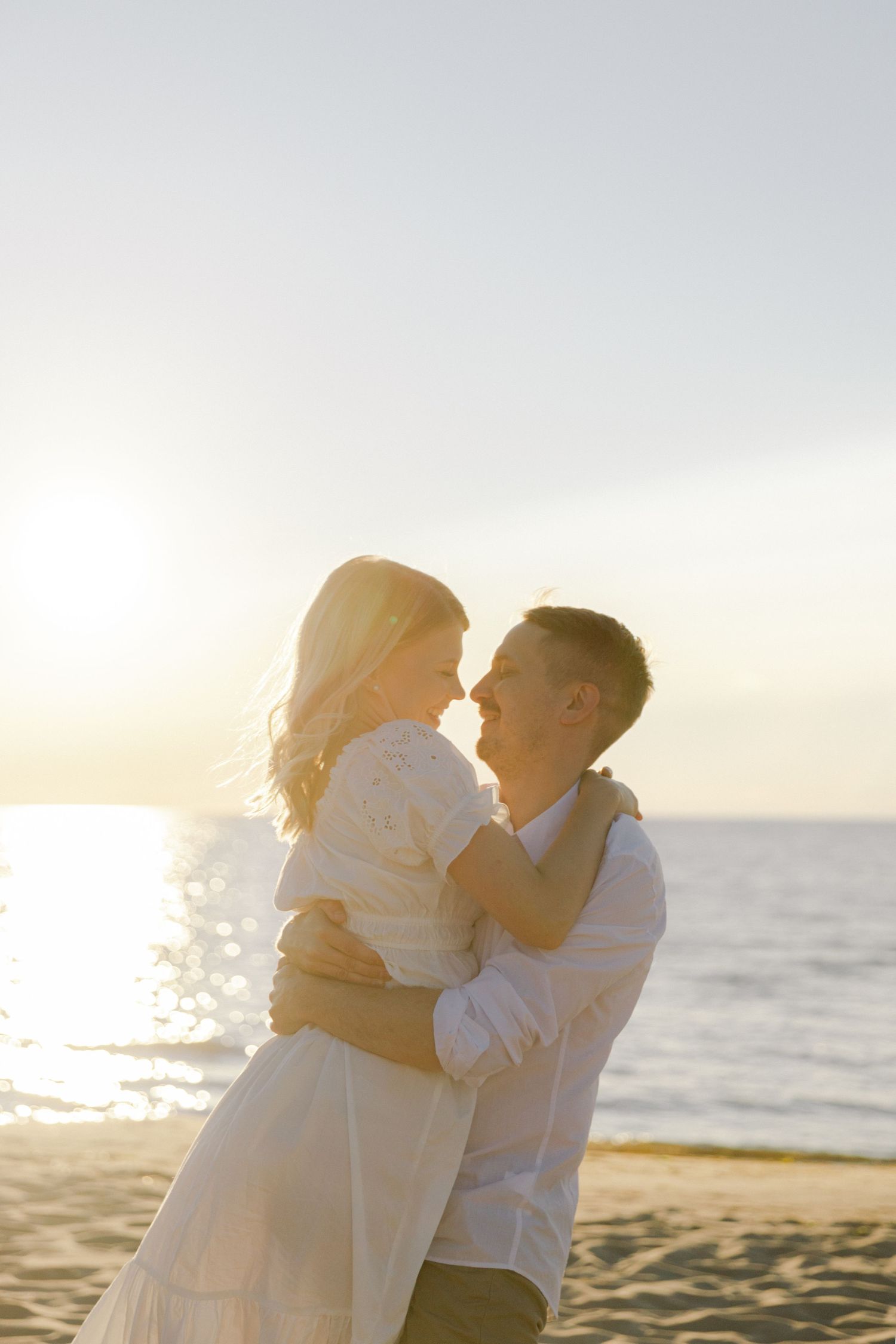 Romantic beach portrait of couple in white clothing at golden hour.