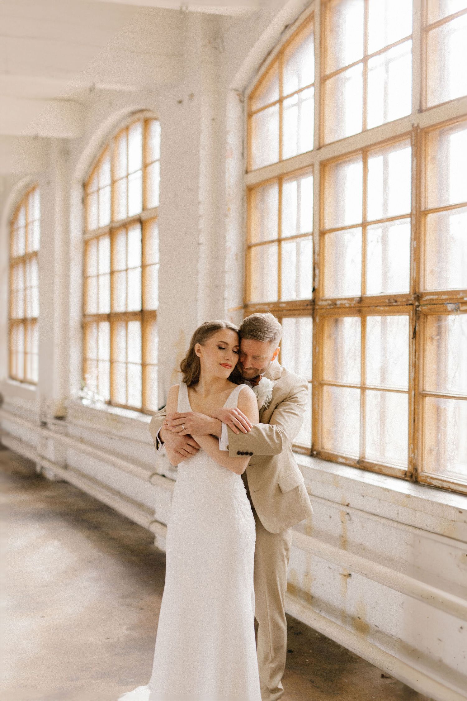 Couple embracing in romantic sunlit room with arched windows.