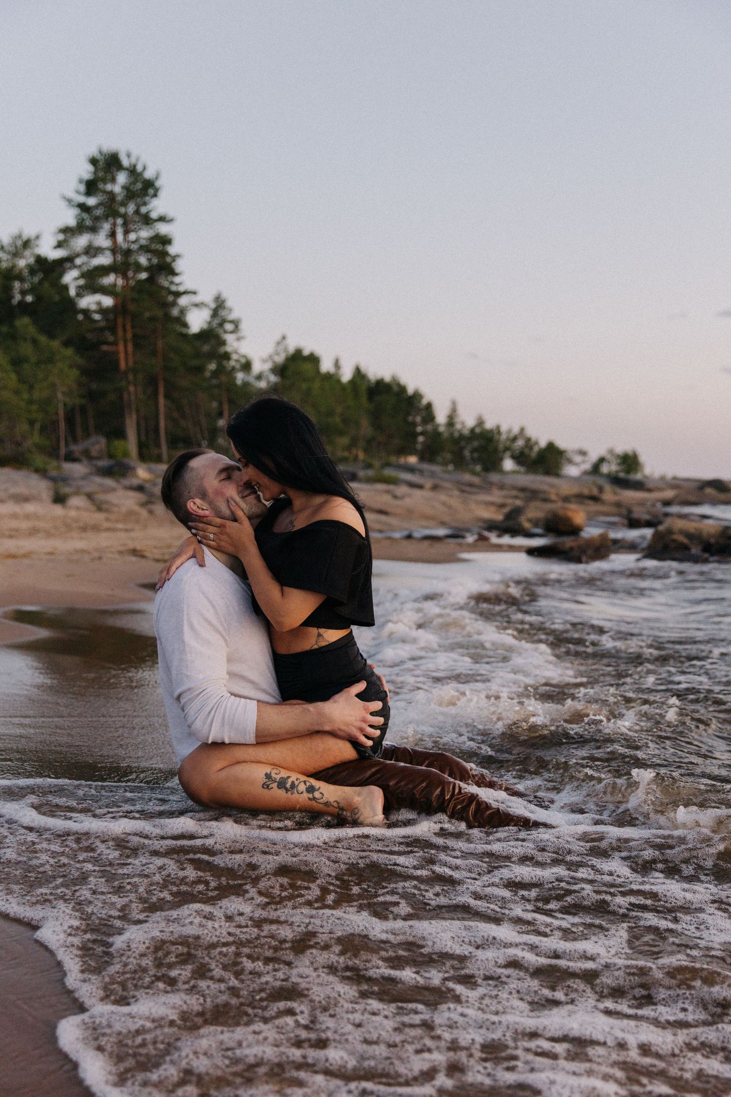 Intimate moment between couple in waves at rocky beach.