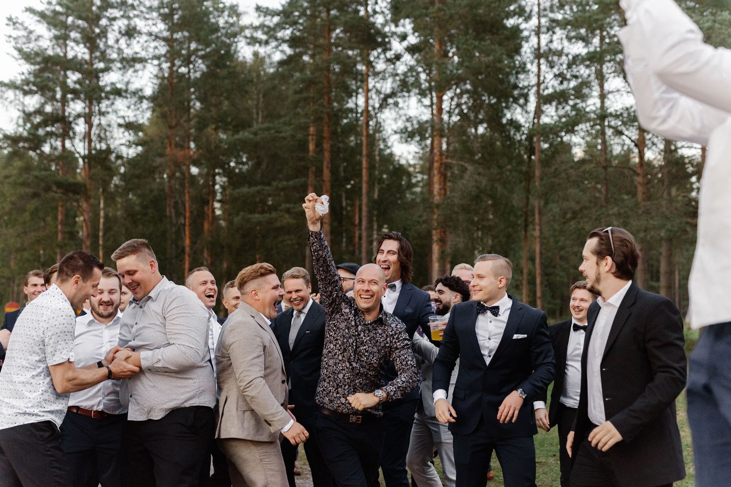 A group of wedding guests gathered outdoors among tall pine trees for a celebration shot.