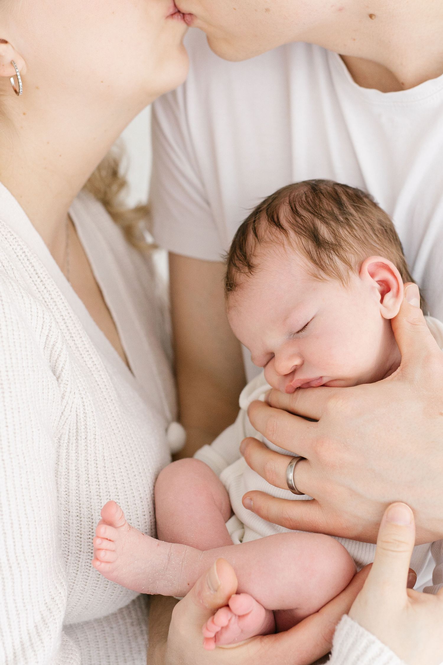 Intimate family moment with sleeping baby cradled between parents.