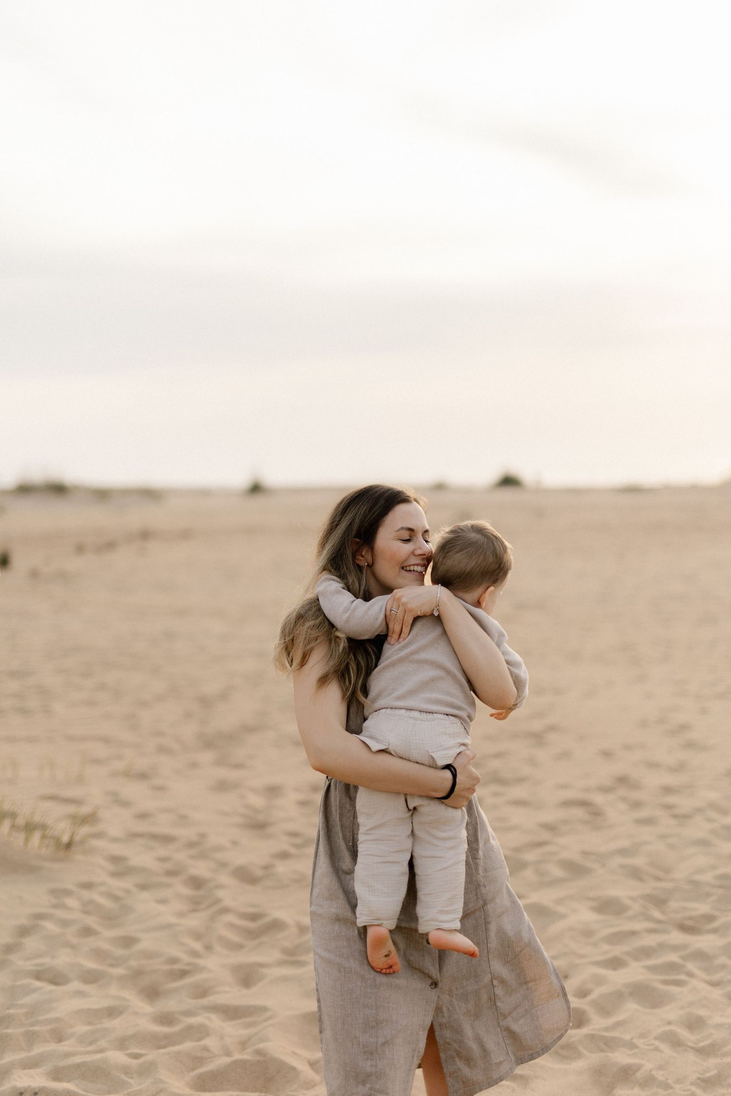 Joyful embrace between parent and child on sandy desert landscape at dusk.