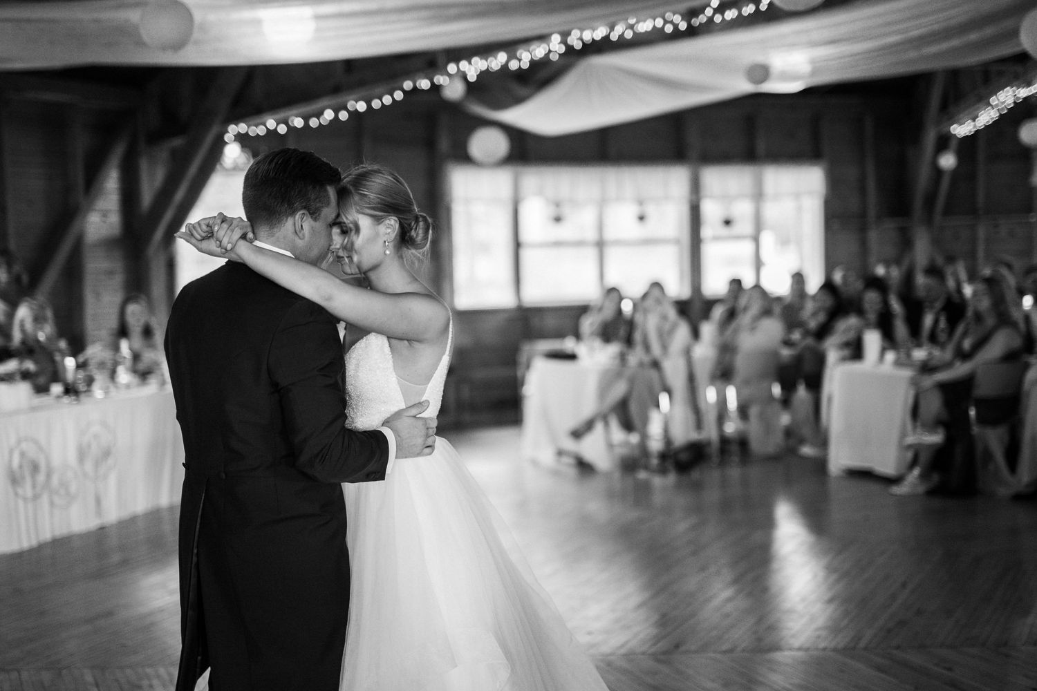 Couple sharing their first dance in a dimly lit reception hall with guests in the background.