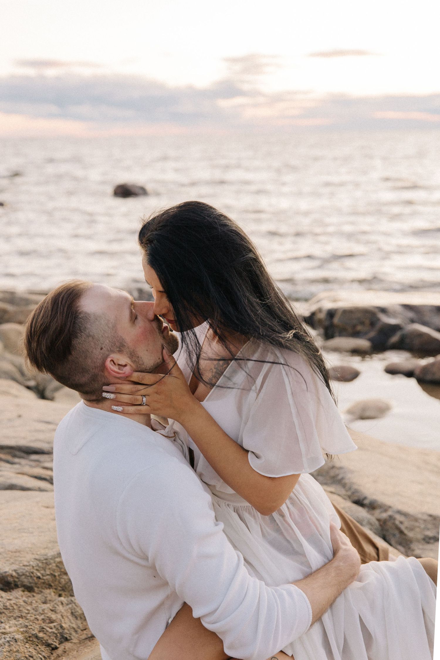 Romantic couple sharing passionate kiss on coastal rocks during sunset.