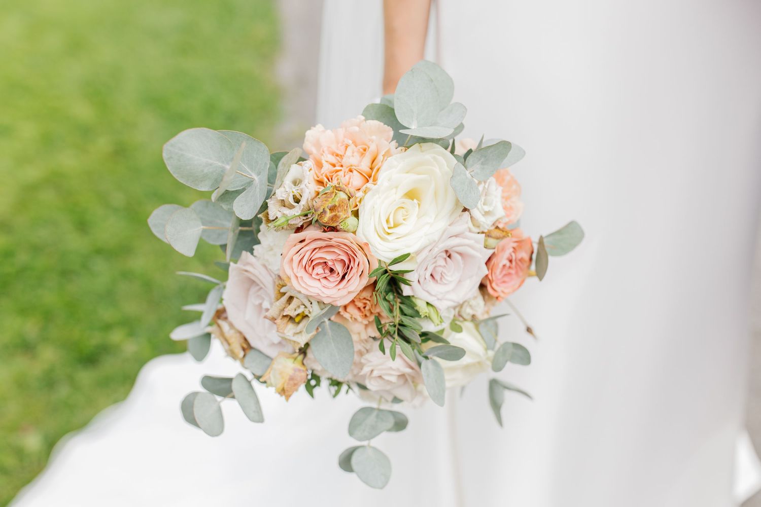 A romantic wedding bouquet featuring peach and cream roses with silver-dollar eucalyptus foliage.