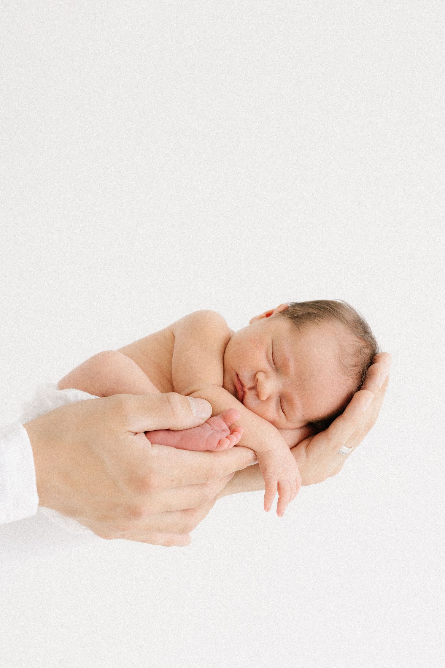 A sleeping newborn baby wrapped in white fabric lying peacefully against a light background.