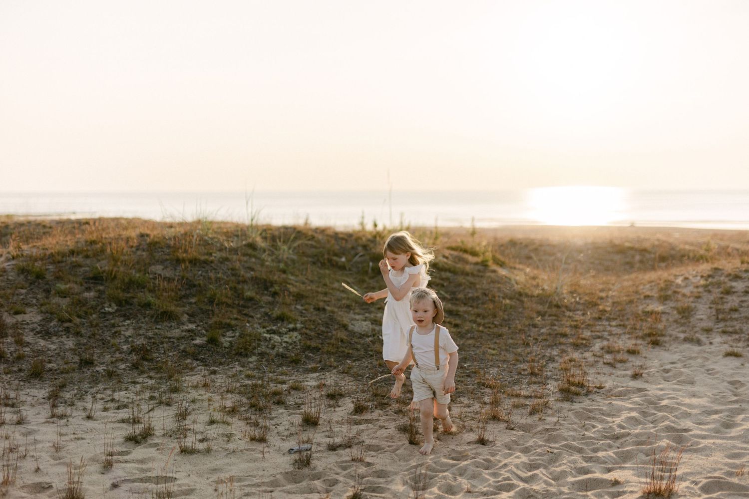 Silhouetted figures walk together up a sandy hill during golden hour.