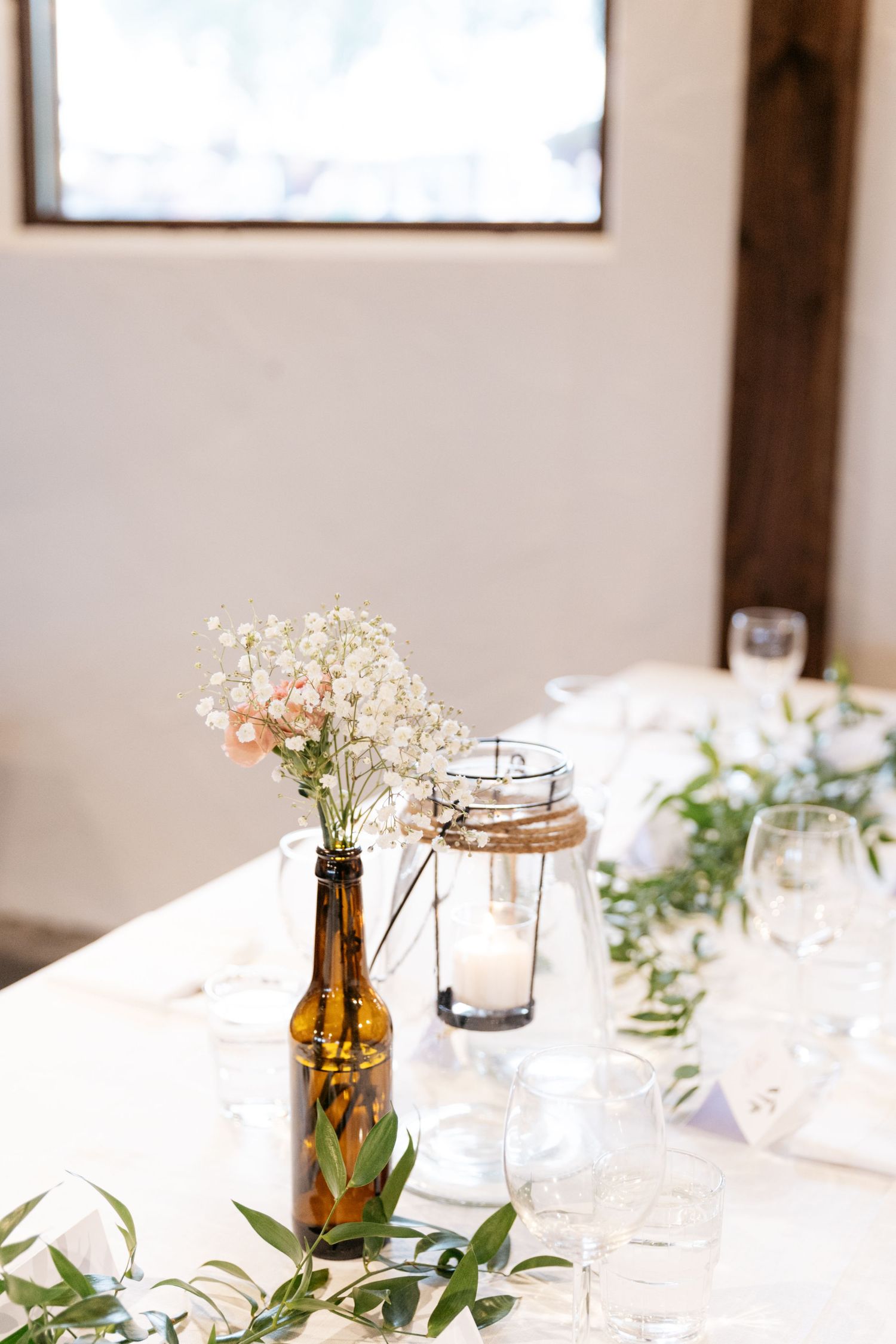 White wildflowers in an amber bottle serve as rustic wedding table decor with greenery and glass jars.