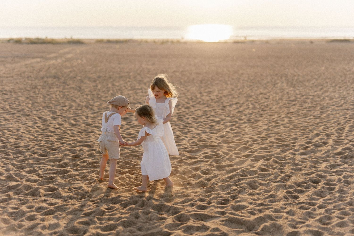 Two people in white dresses dance together on a beach at sunset.