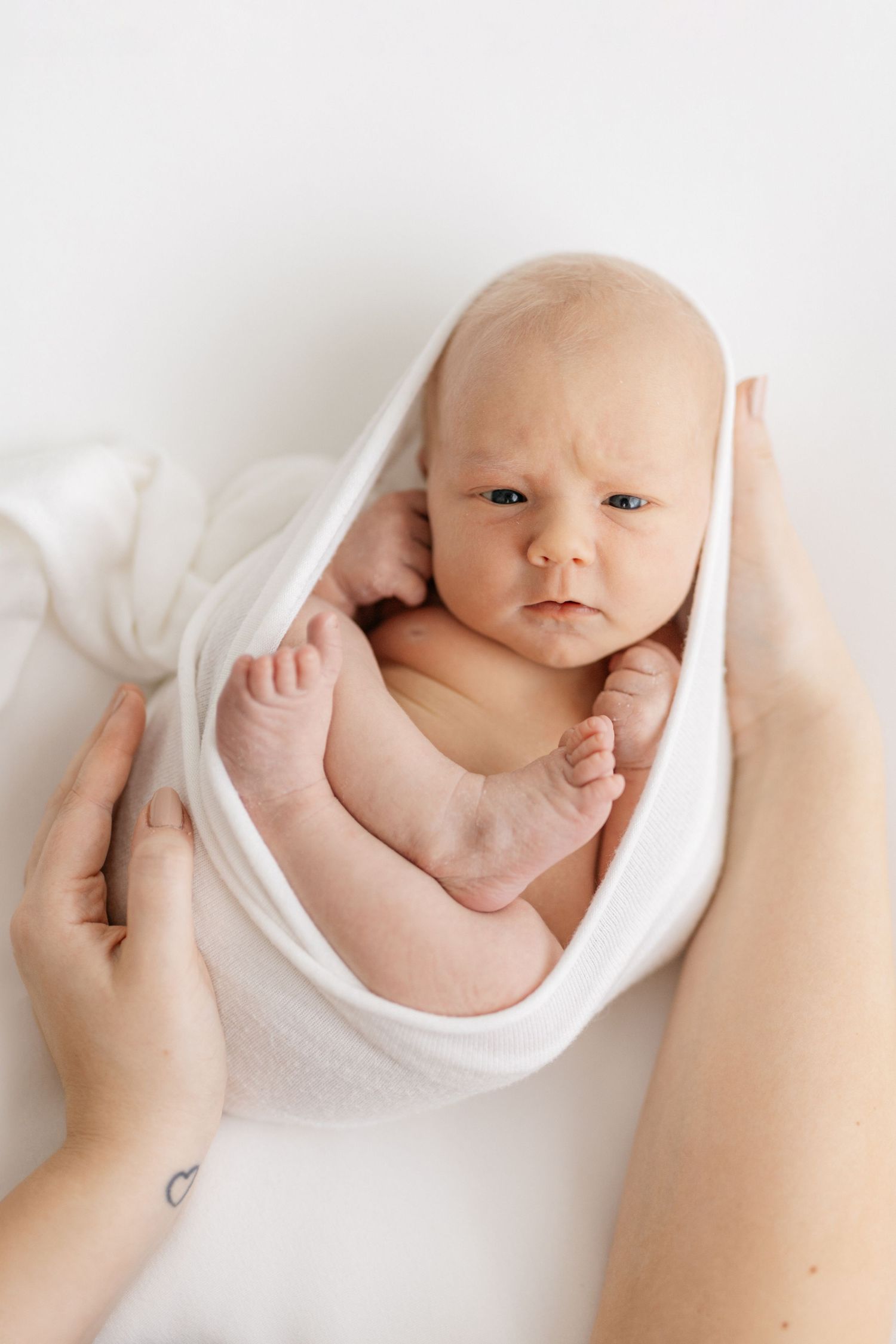 Sweet newborn baby wrapped in white blanket during minimalist photo session.