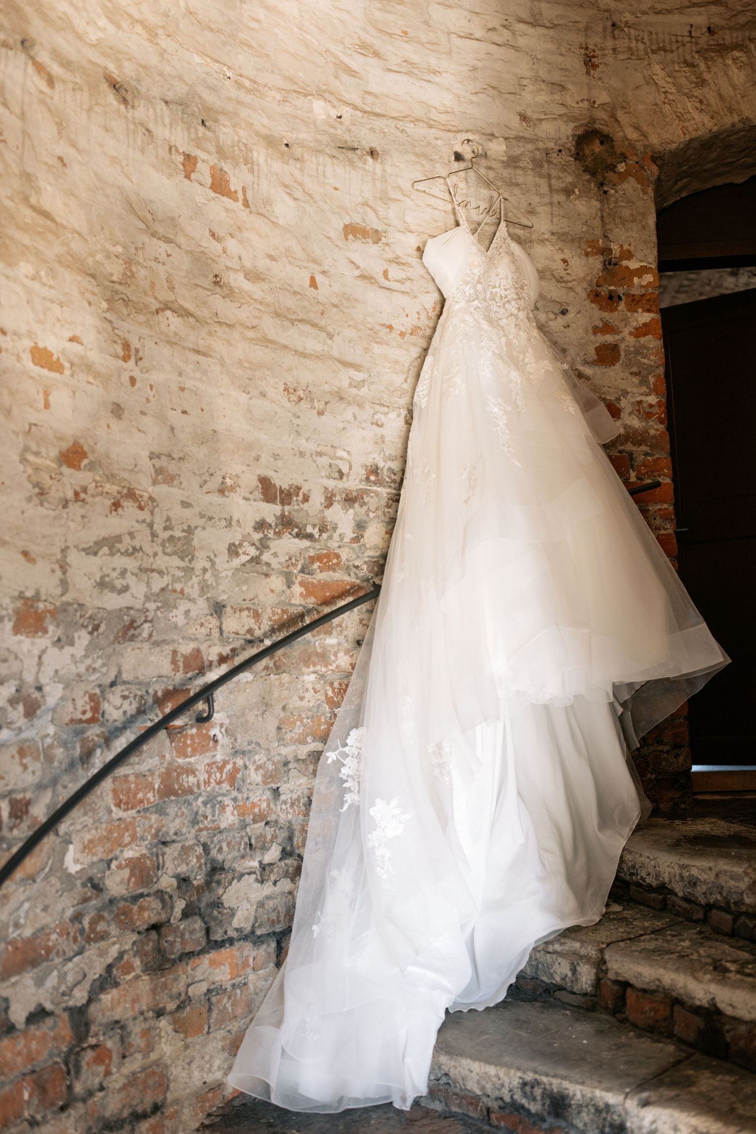 Elegant white wedding dress hanging on rustic brick wall with flowing tulle skirt.