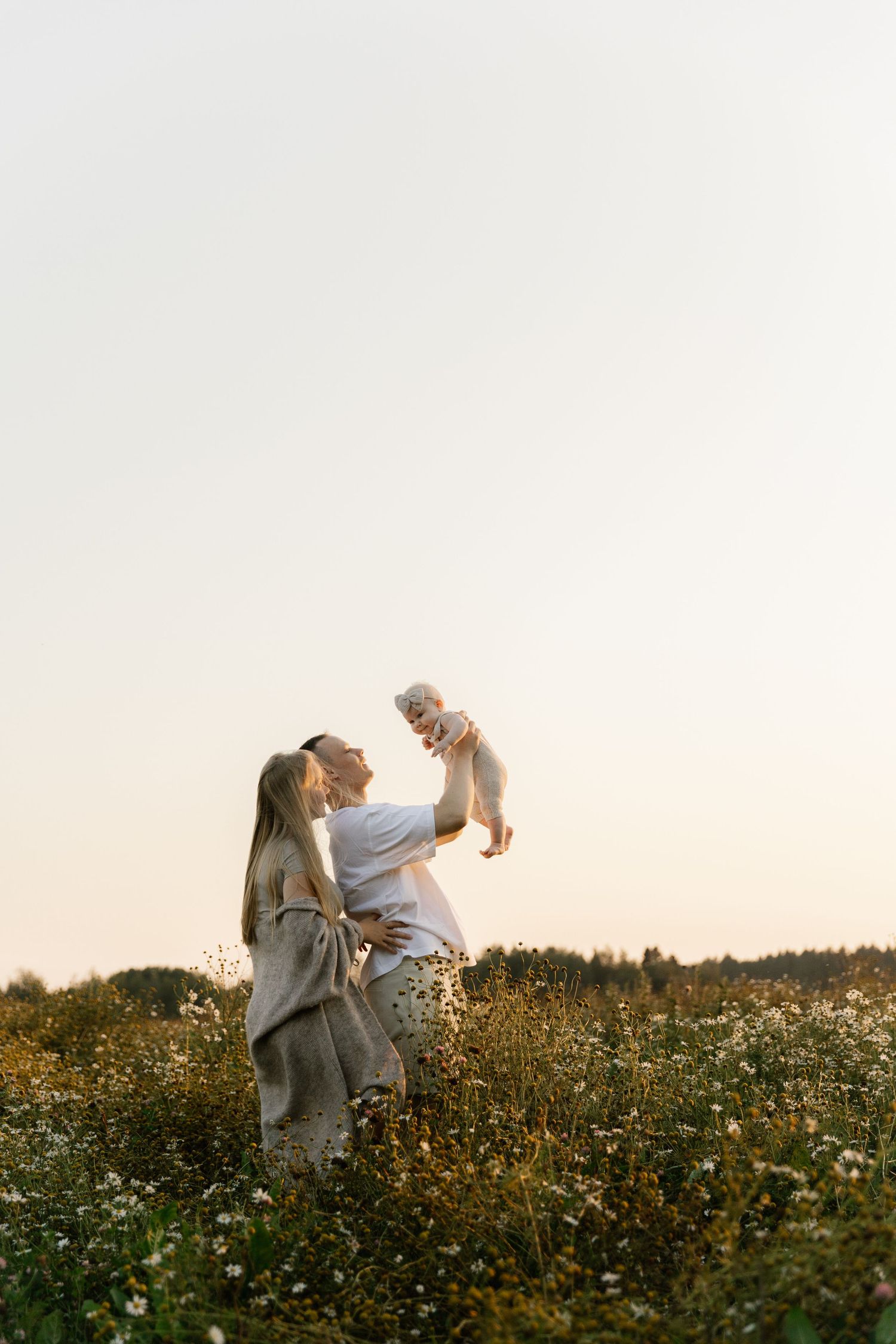 Parents playing with baby in wildflower meadow during sunset.