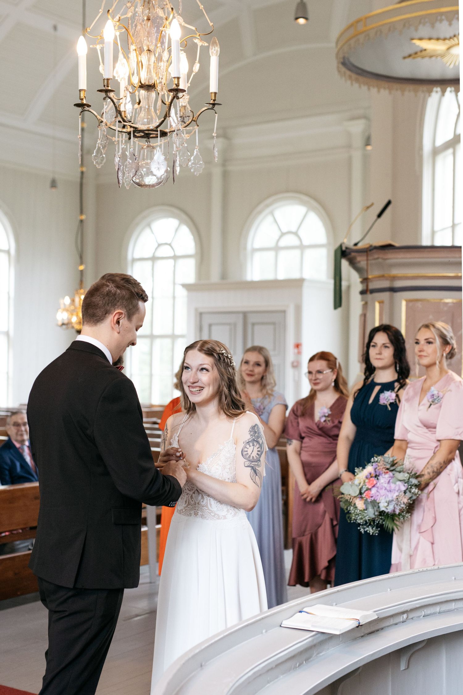 Wedding ceremony moment in a bright church interior with elegant chandelier and gathered guests.