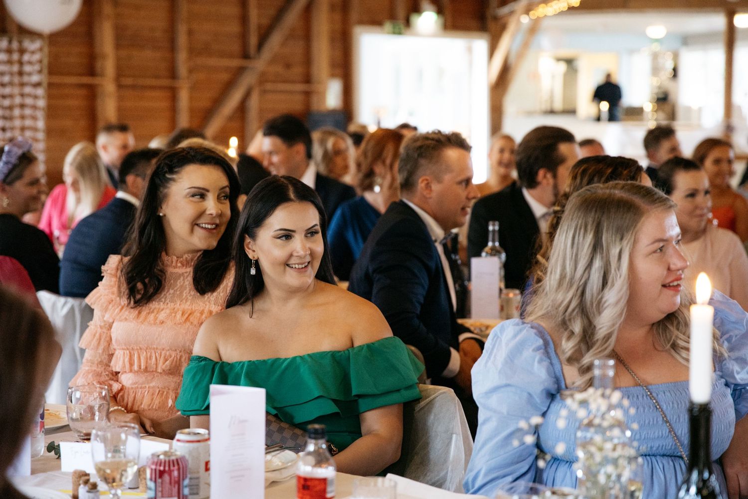 Wedding reception guests enjoying themselves at tables inside a rustic barn venue.