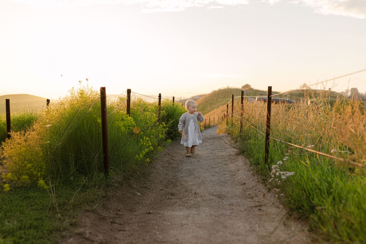 Two figures in light colored dresses walk down a rural path at sunset.