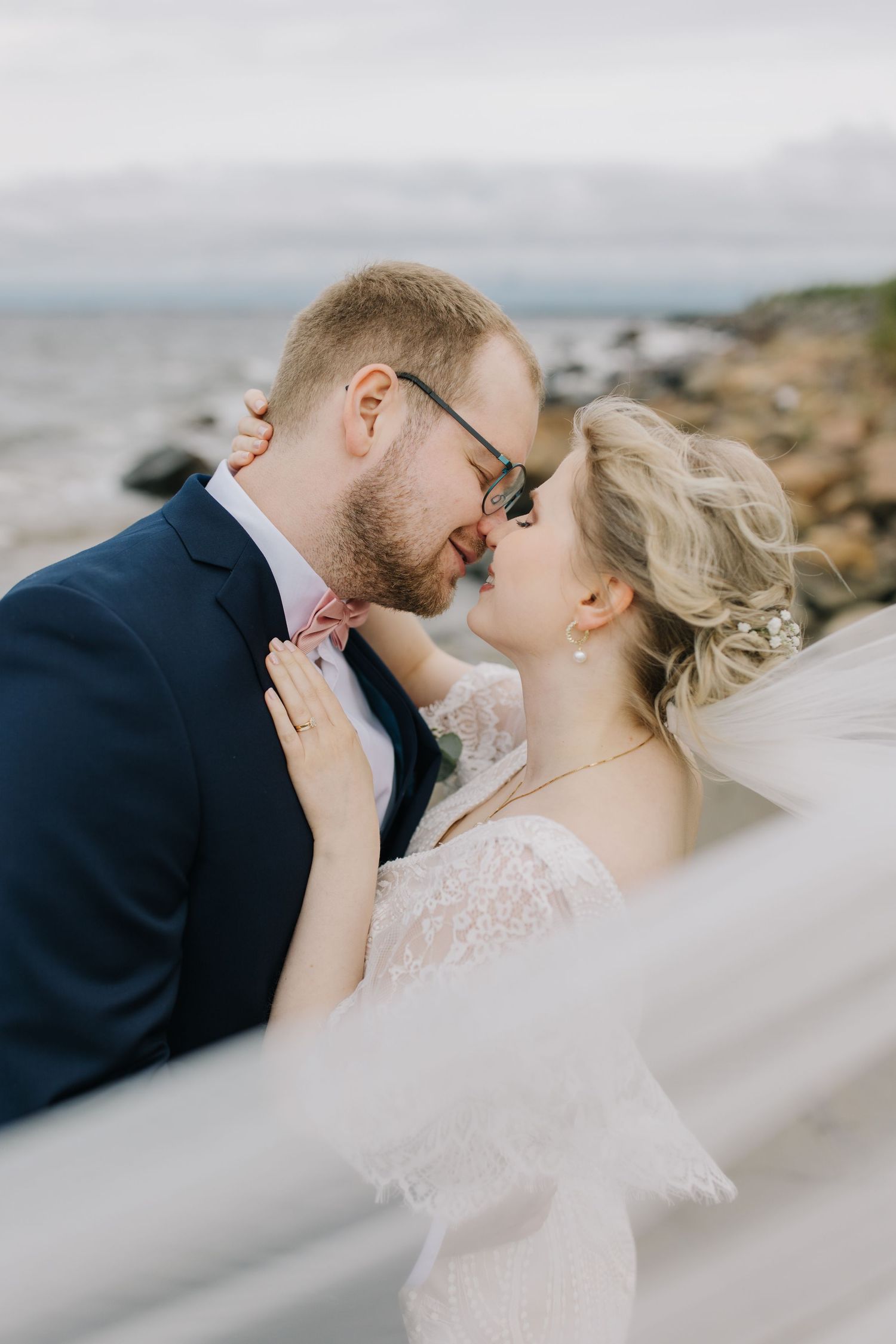 Romantic seaside wedding portrait with couple sharing an intimate moment against a cloudy coastal backdrop.