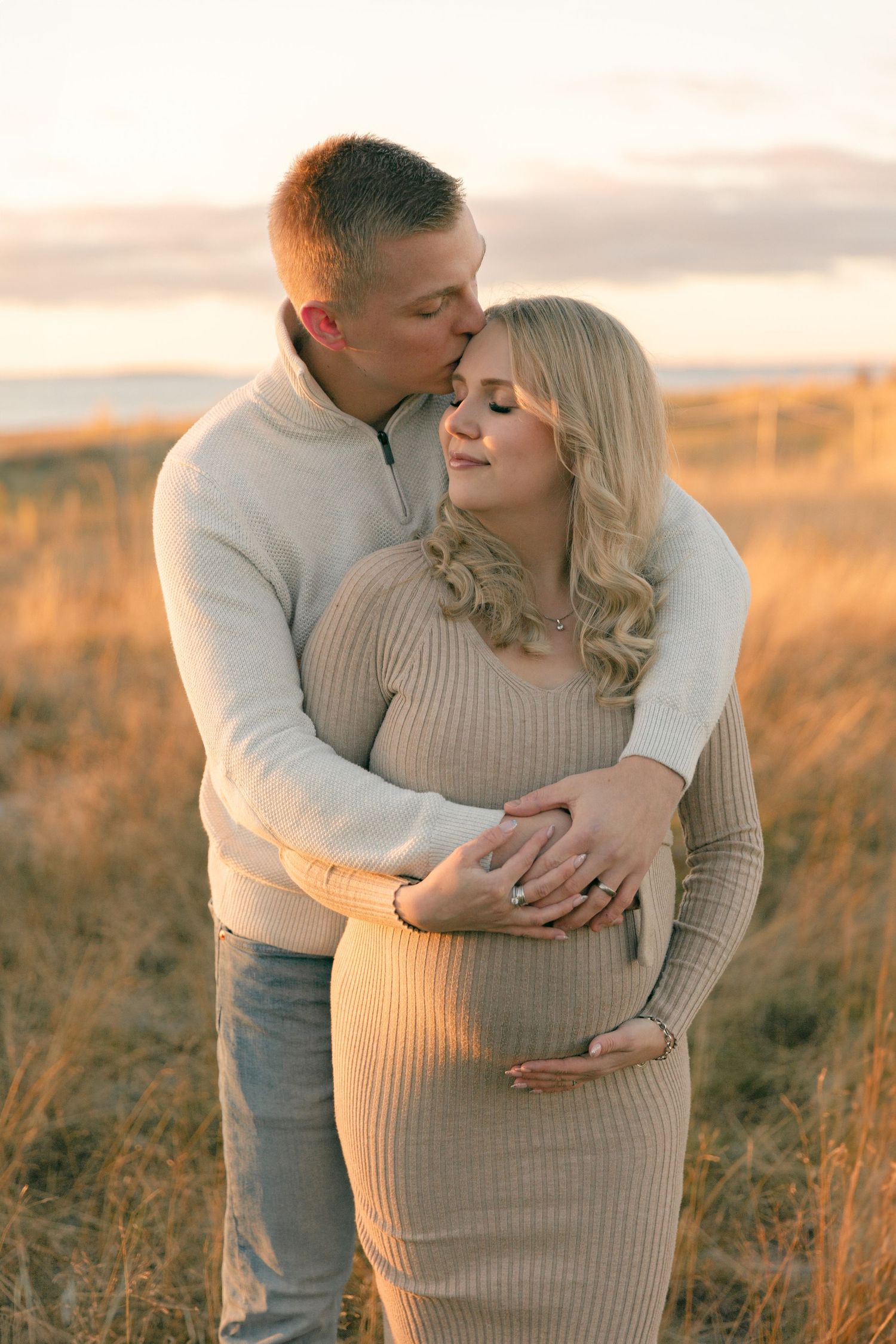 Intimate maternity portrait of couple embracing in golden field at sunset.
