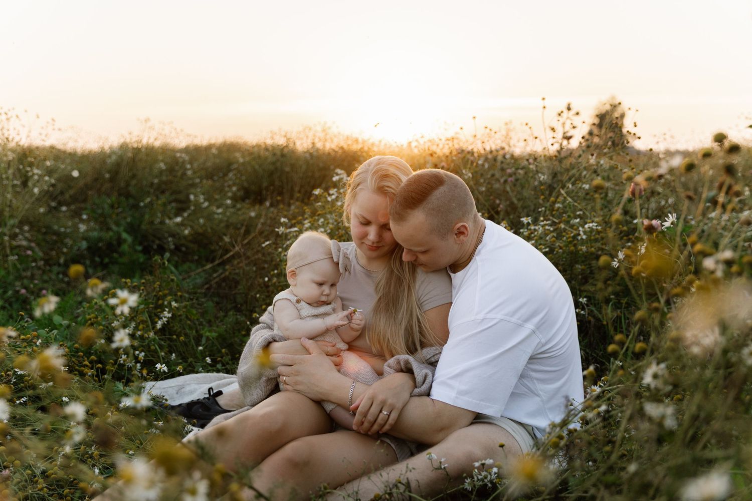 Family sitting together in blooming wildflower field at sunset.